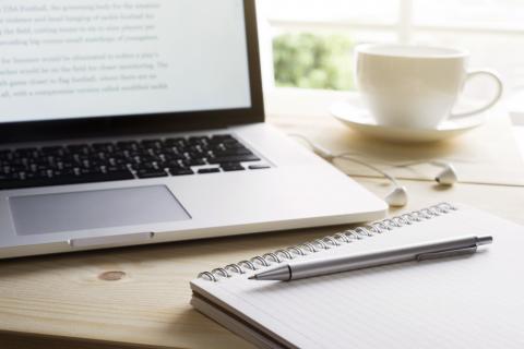 a laptop and a notebook sit on top of a table next to a cup of coffee or tea