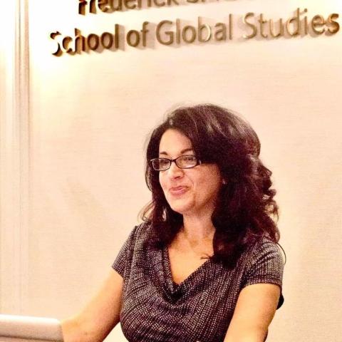 Photo of a dark-haired woman with glasses standing at a podium.