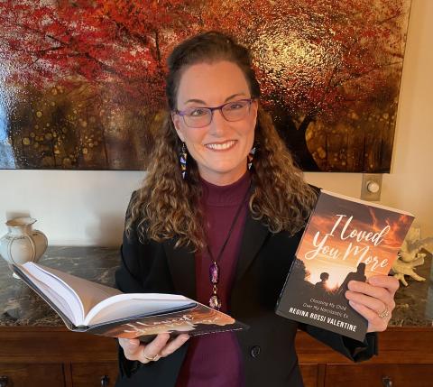 A woman with long hair and glasses holds copies of her new book, one in each hand. The book in her right hand is open. The book in her left hand is held so that the front cover is visible.