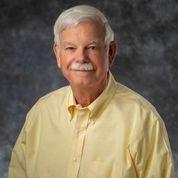 Photo of an older man with gray hair & a gray moustache, wearing a yellow shirt.