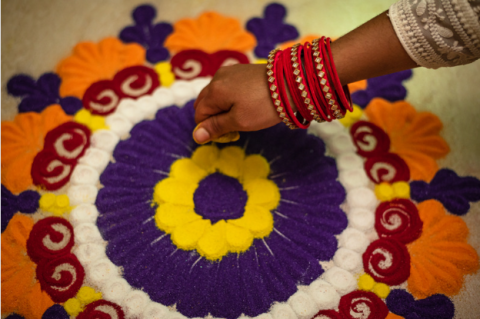 Hand completing a rangoli design with colored sand