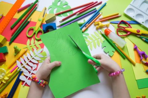 Hands using scissors to cut out paper with crafts in the background