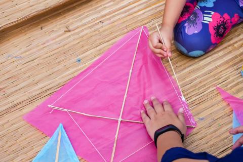 A pink kite being worked on by a child's hands while an adult's hands holds it steady.