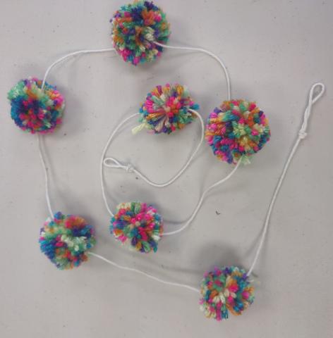 Several pom-poms made of yarn are strung on a string into a garland.