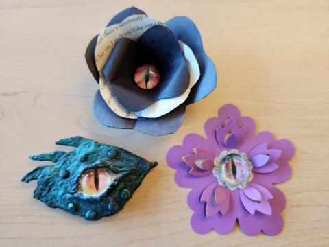 Green clay dragon eye, black and white paper flower with dragon eye, and purple paper flower with dragon eye.