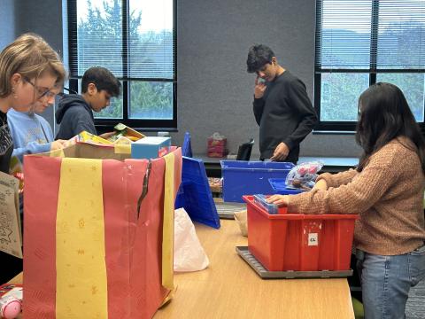 Image of teens at a table sorting toys into boxes. 