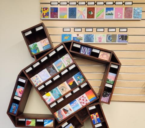 Man-shaped bookshelf containing various artwork on tiny canvases.