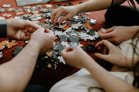 several pairs of hands moving jigsaw puzzle pieces