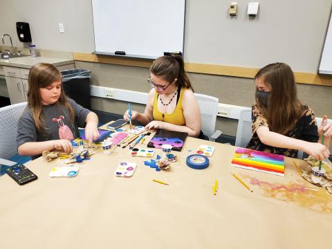 Three teen girls painting small colorful canvases. 