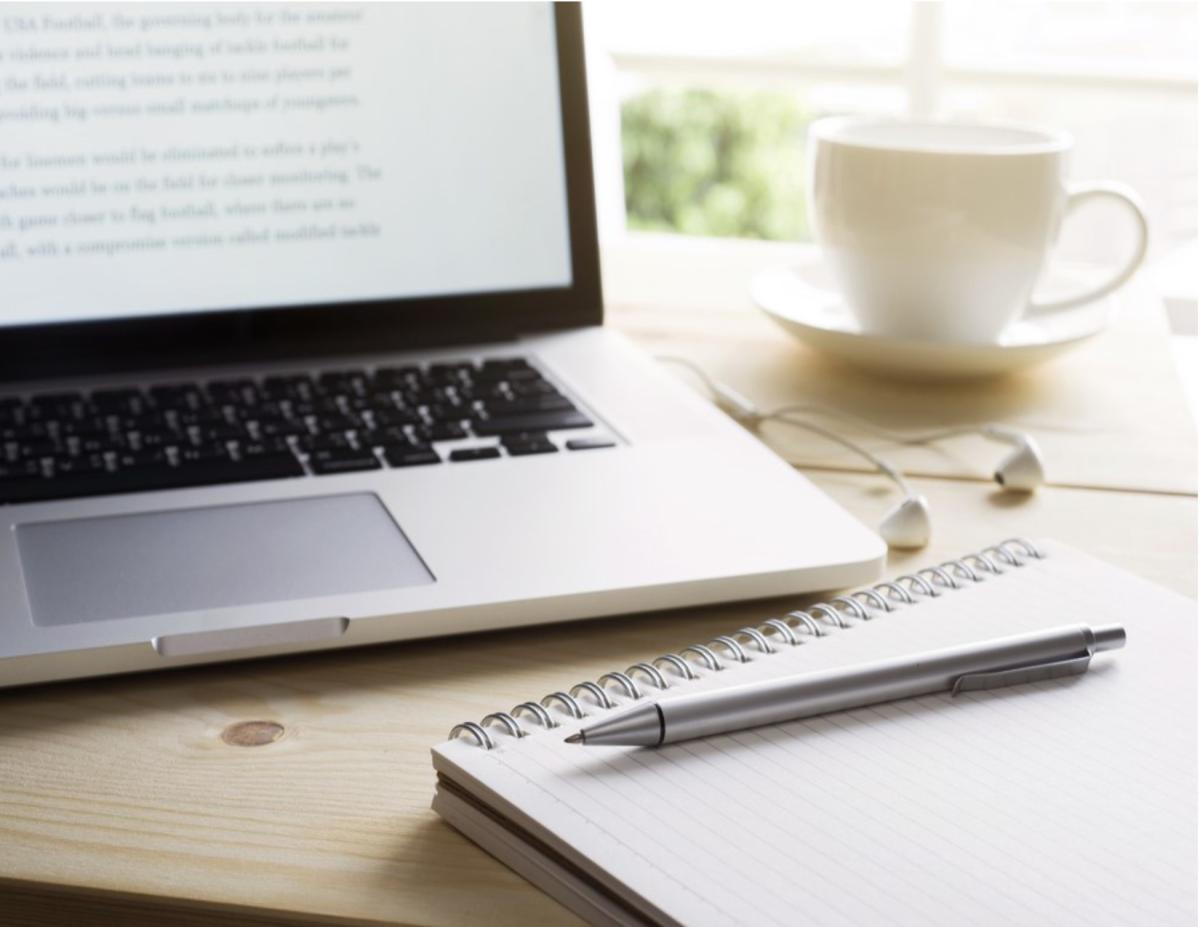 Table with laptop, ear buds, notebook with pen, and coffee or tea cup