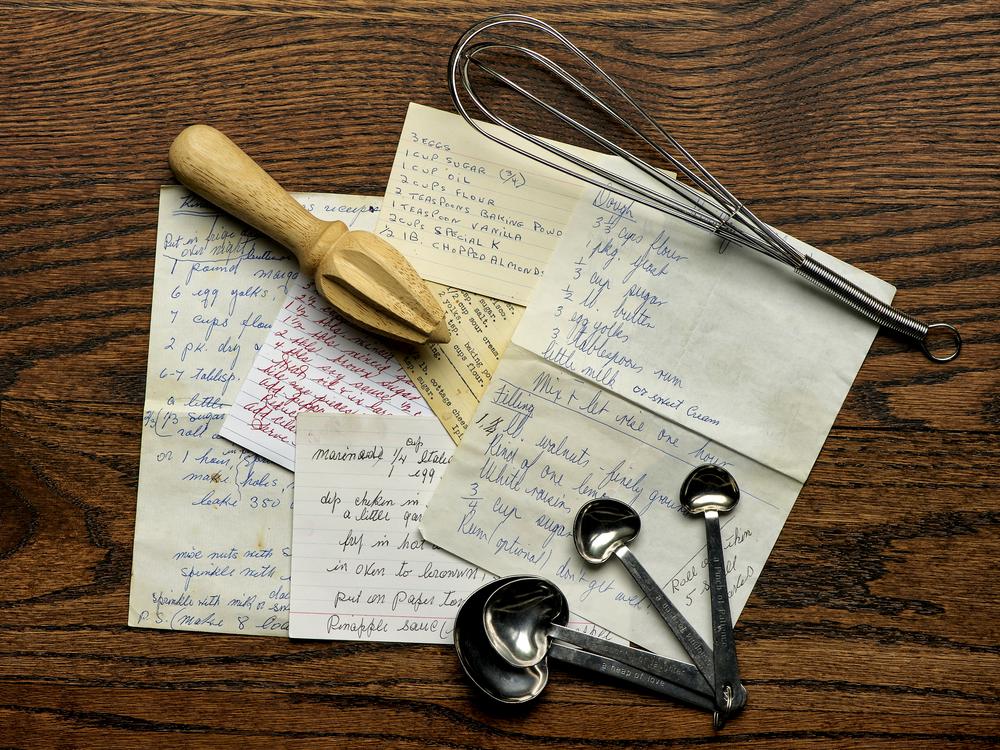 Old recipes with wire whisk and measuring spoons with wooden juicer on wood background