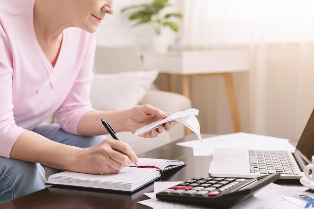 senior lady counting bills and making notes at home