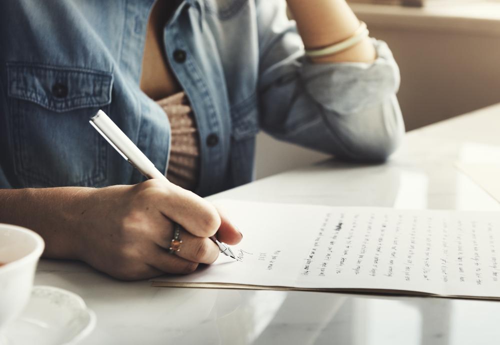 A person writing with pen in hand and paper at desk