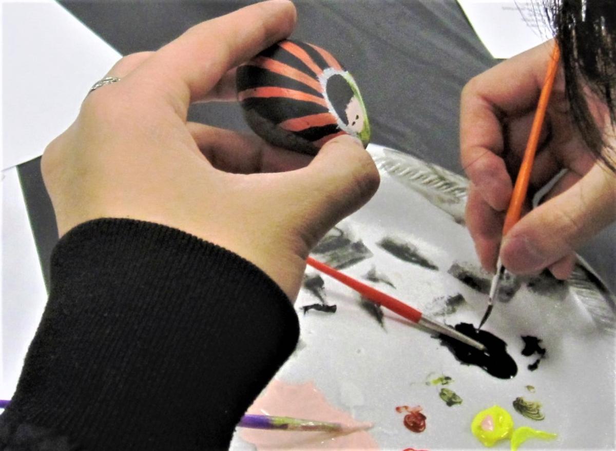 hand holding rock painted with design, other hand holding paint brush