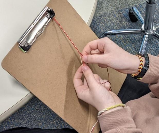 hands making friendship bracelet on clipboard