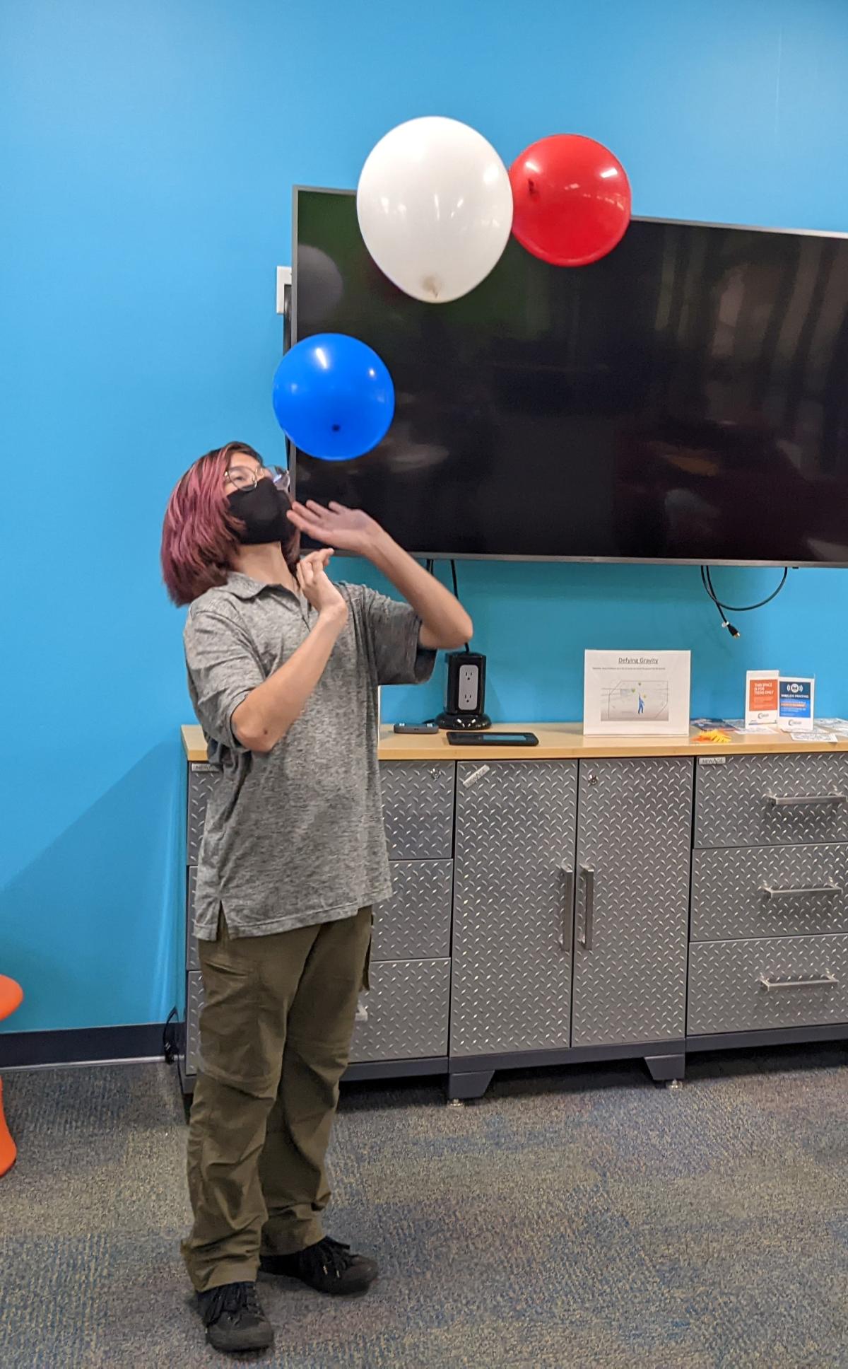 teen keeping blue, white, and red balloons in the air