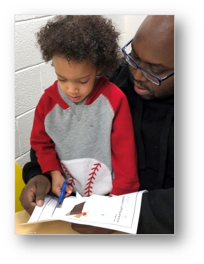 boy cutting with scissors with adult helping