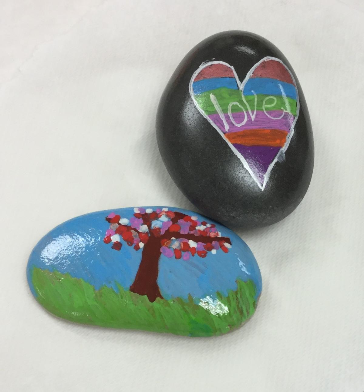 Two rocks painted in different styles. One has a tree on it with a blue background, and the other has a heart on it with love written in the middle of the heart.