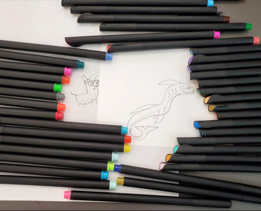 Colorful pens around two drawings: a cricket (left) and a dragon (right)