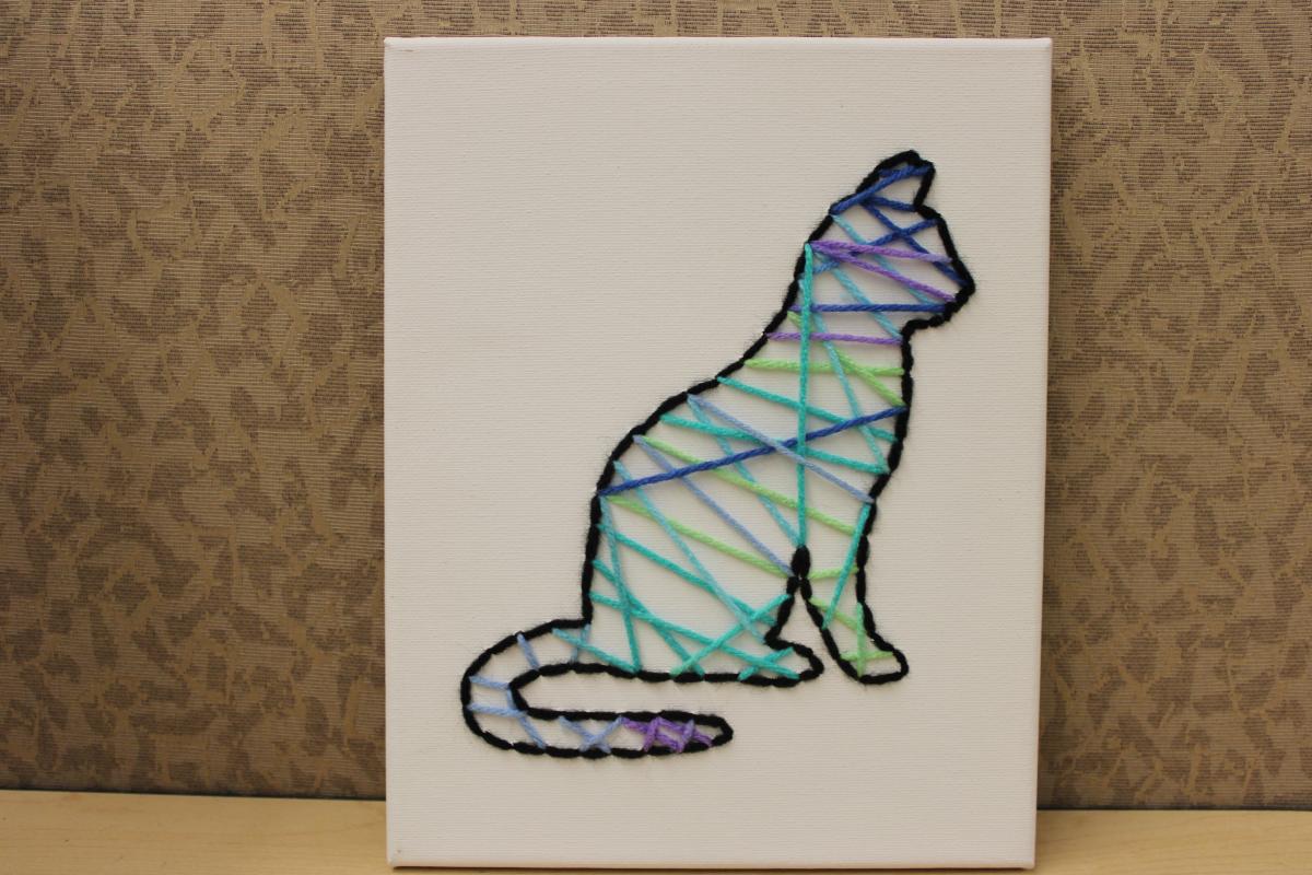 Outline of cat embroidered in black yarn on a white canvas. Multicolor yarn fills in the middle.