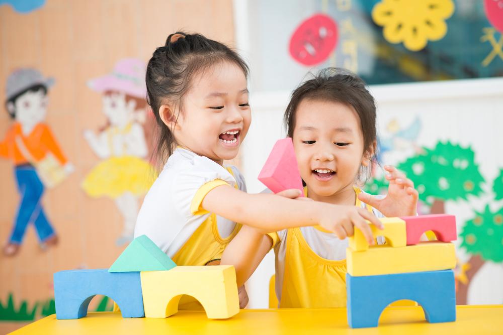 Two young girls playing with colorful blocks in a classroom