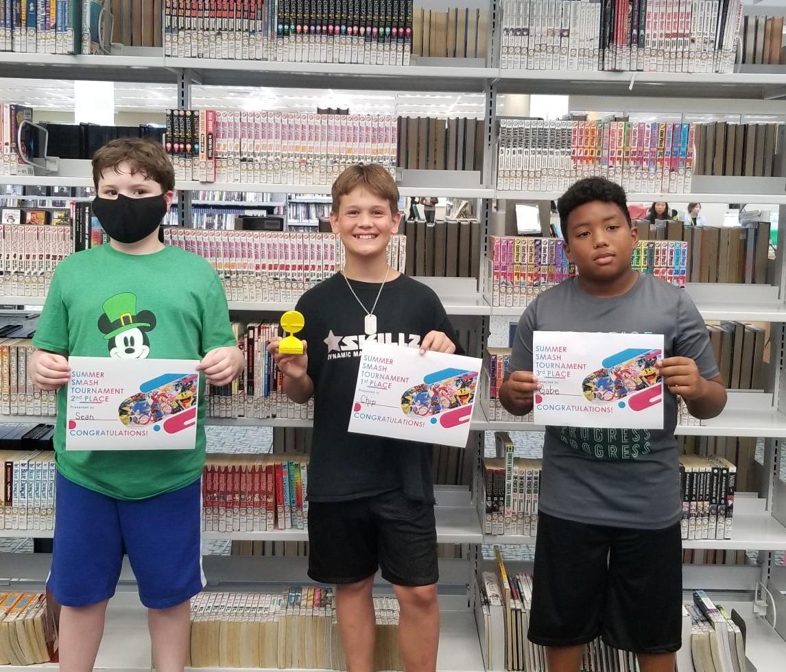 Three tween boys holding certificates and smiling or looking at the camera.