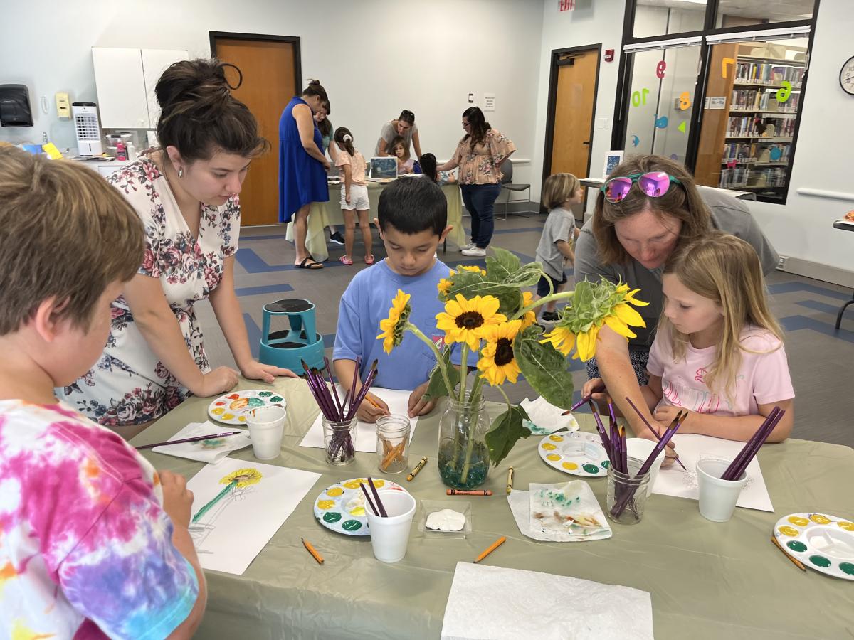 Families doing a library craft together, painting sunflowers.