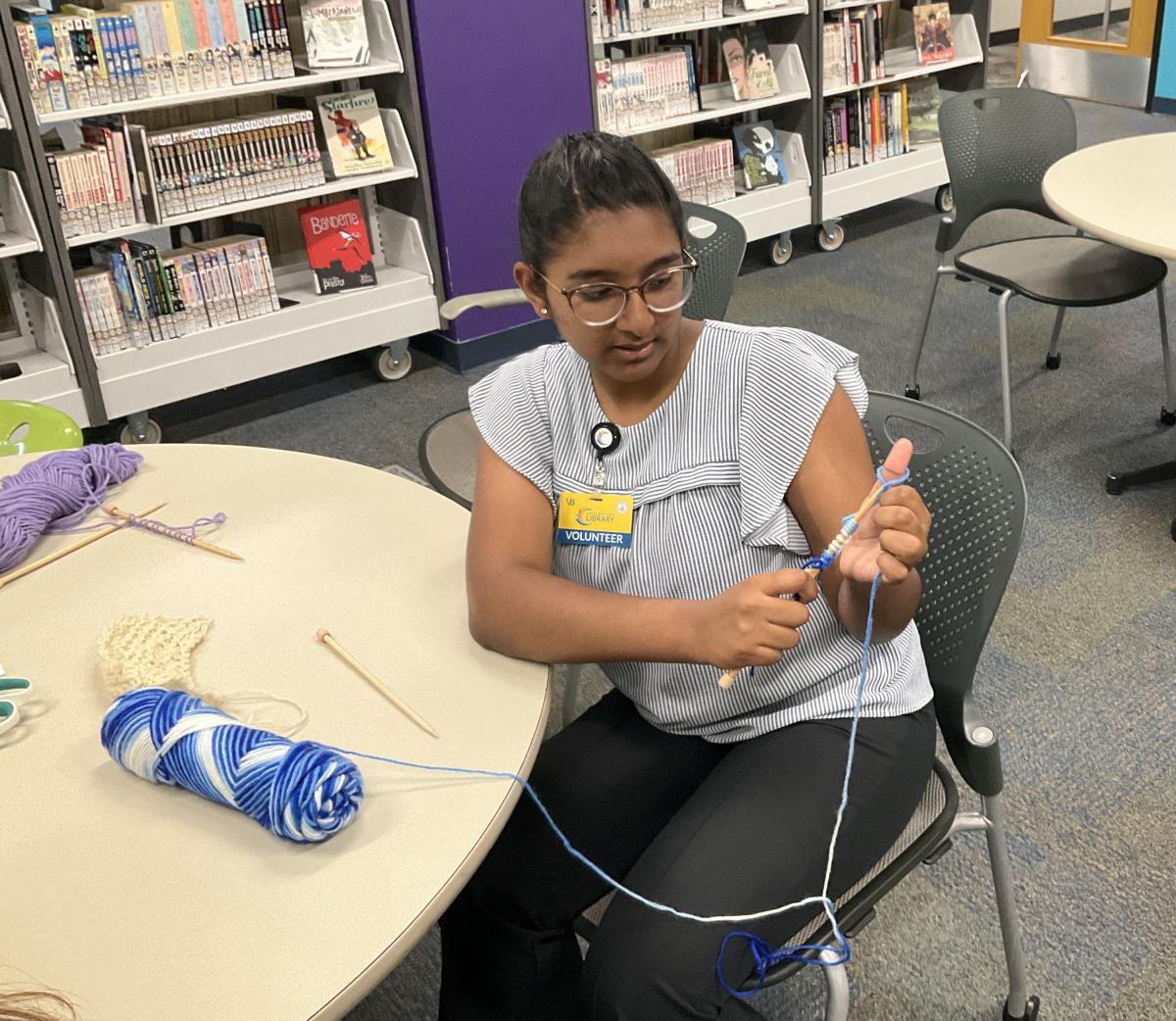 Teen girl knitting with blue and white yarn.