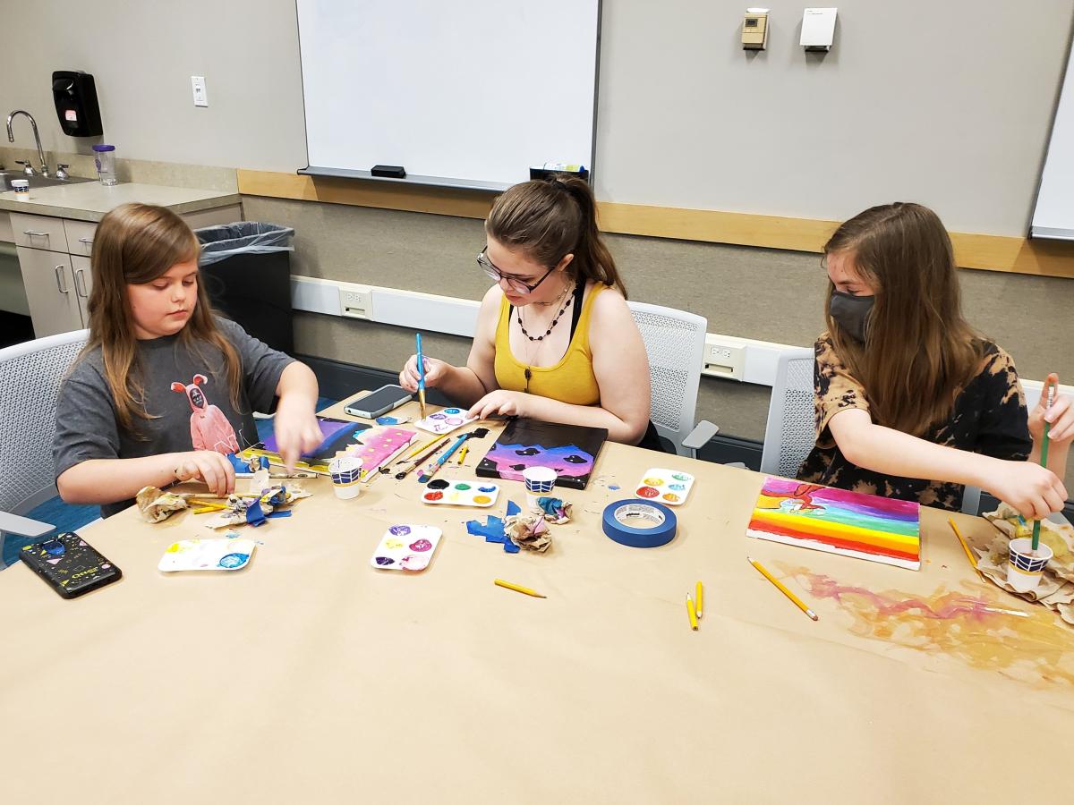 Three teen girls painting small colorful canvases. 