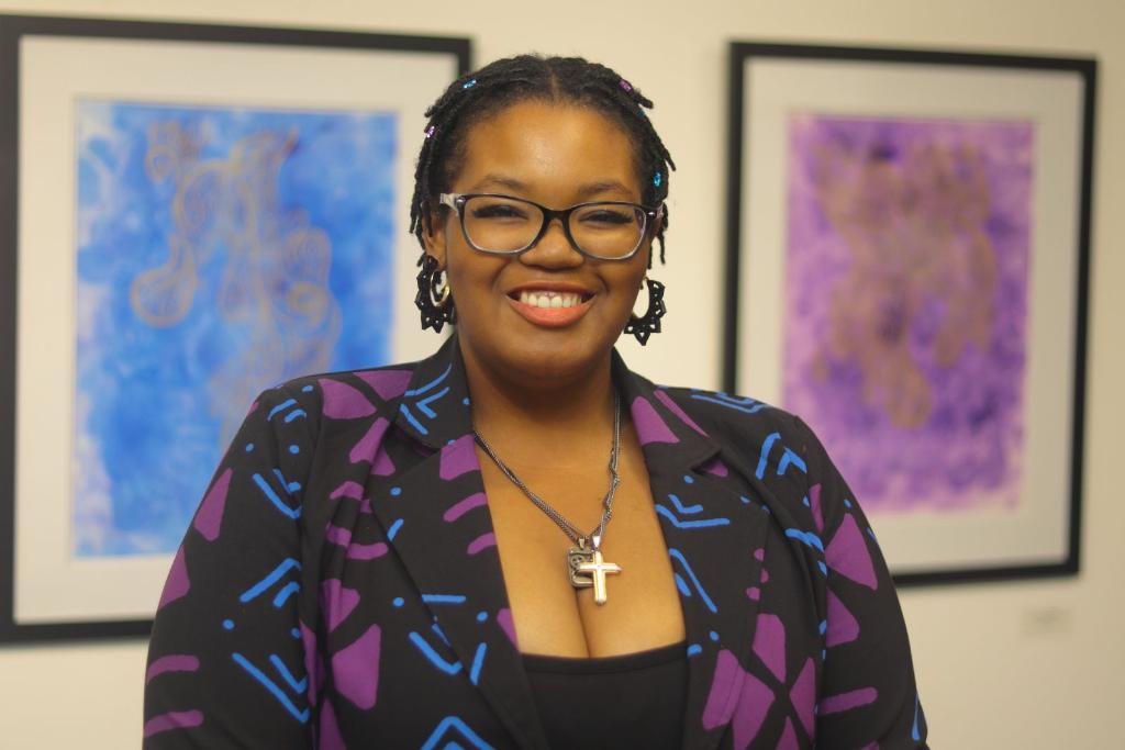 Artist Asiko stands in front of two pieces of her artwork at NSU